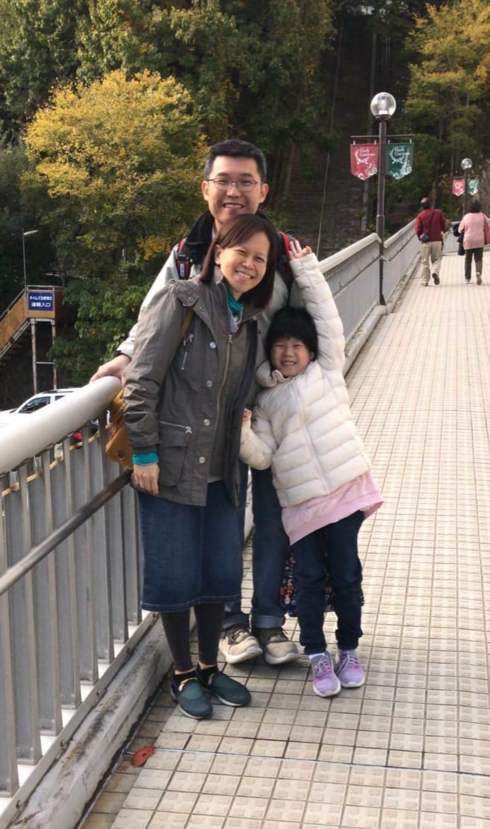 Three people, a man, woman, and young girl, smile together on a tiled pedestrian bridge.